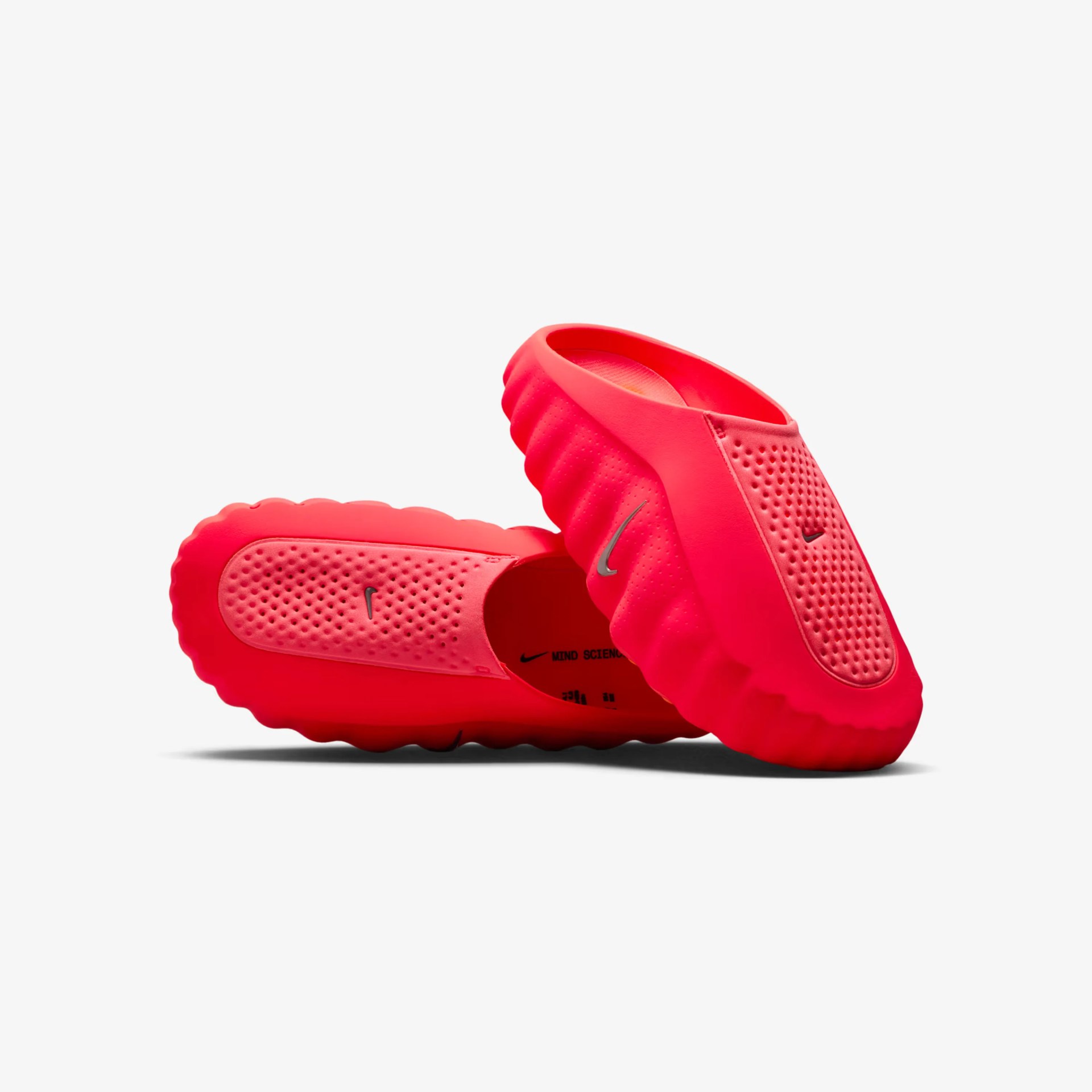 Bright red slip-on shoes with textured uppers and wavy soles, featuring small black Nike swoosh logos.
