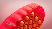 Close-up of a red Nike soccer cleat sole with orange studs and a silver Nike swoosh.