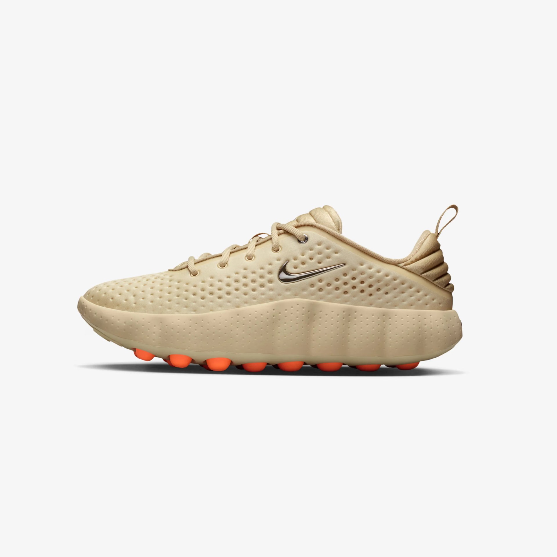 Beige Nike sneaker with perforated upper, metallic swoosh logo, and orange circular outsole studs.