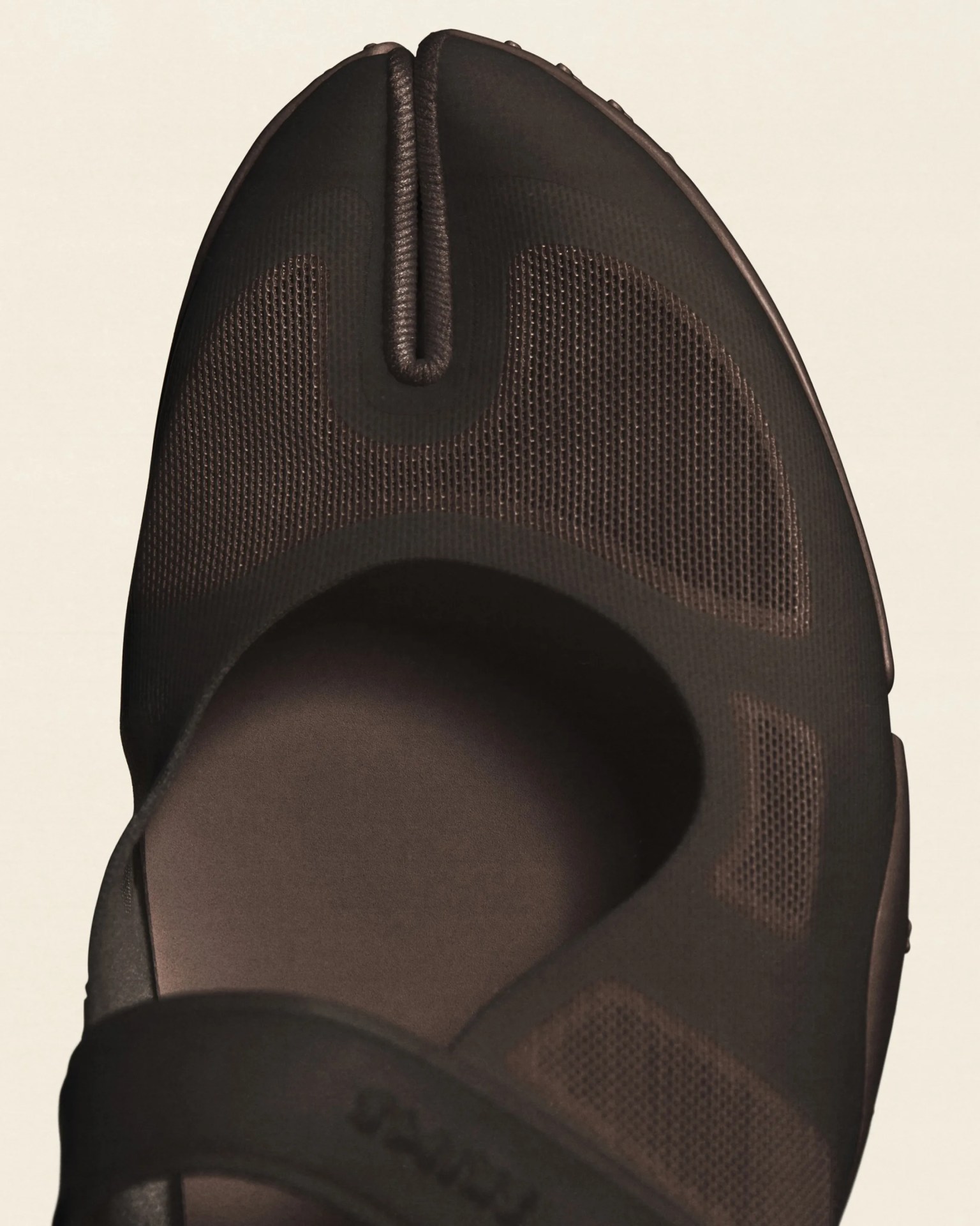 Close-up of a dark brown sandal with a split-toe design and mesh fabric upper.
