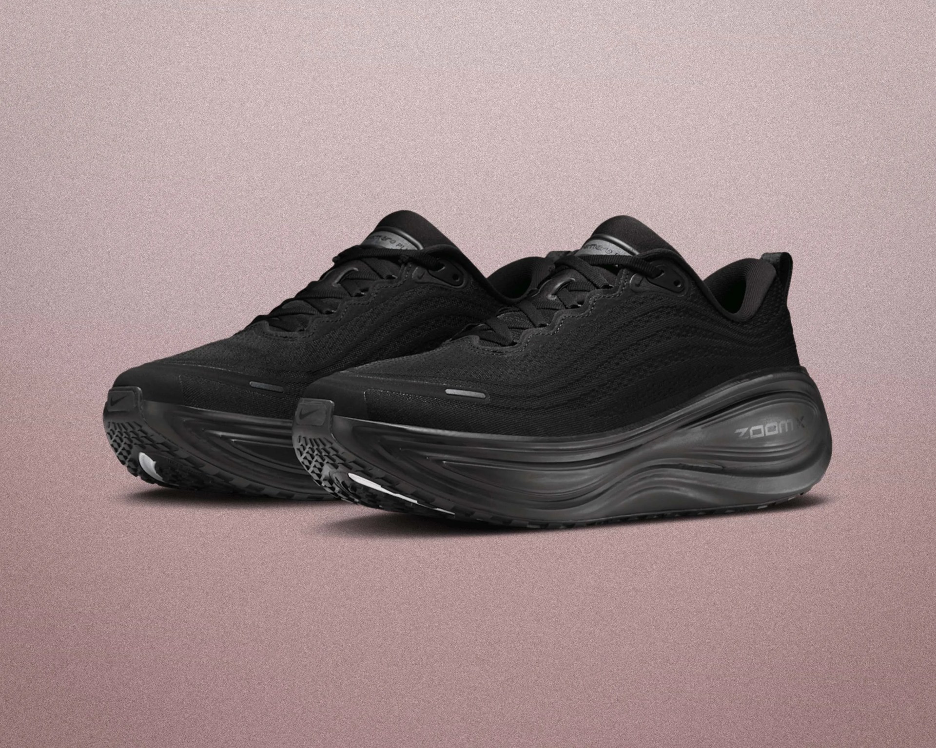 Pair of black Nike ZoomX running shoes with textured mesh upper and thick cushioned sole on a pink surface.