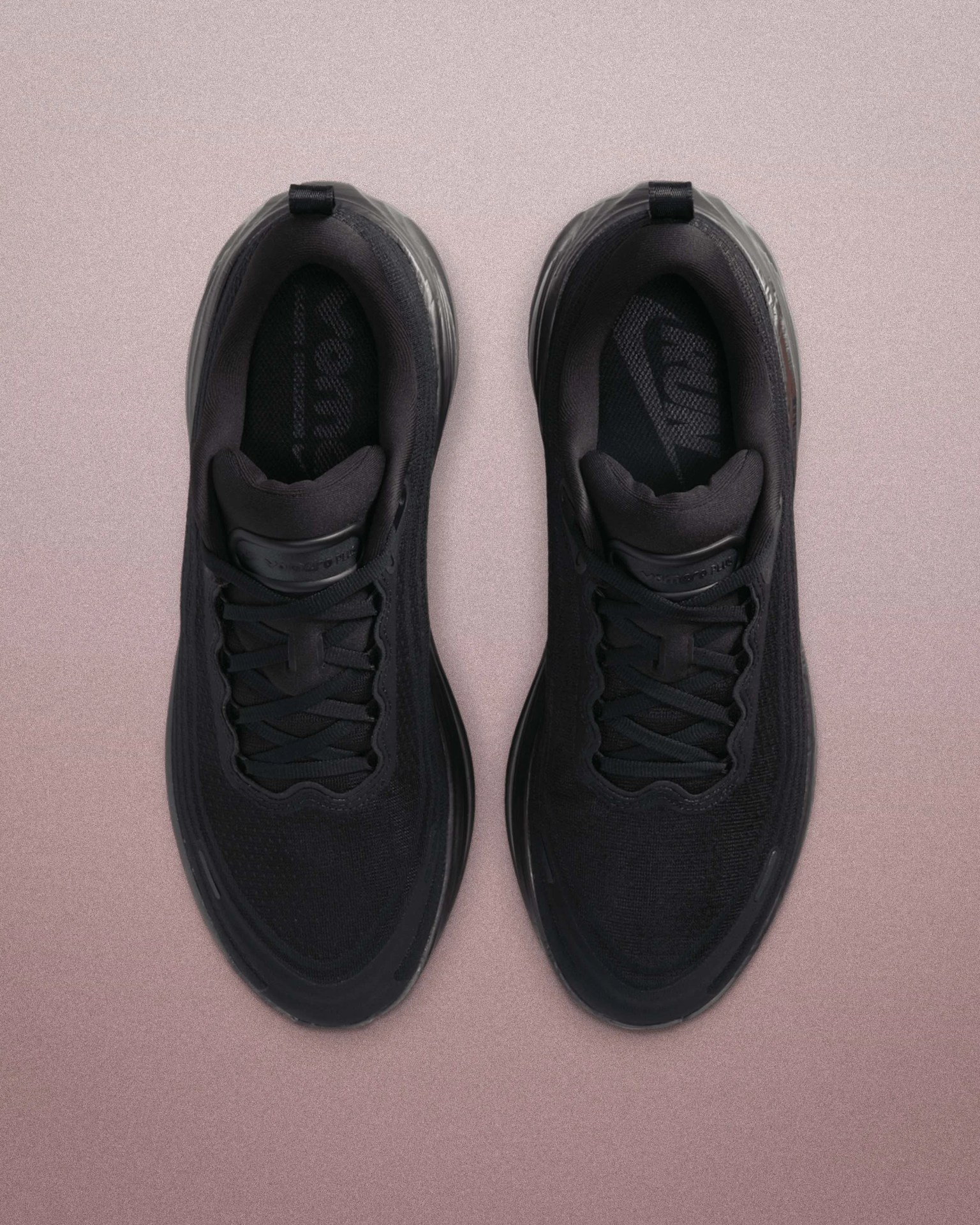 Pair of black athletic shoes with mesh uppers and black laces on a pink textured surface.