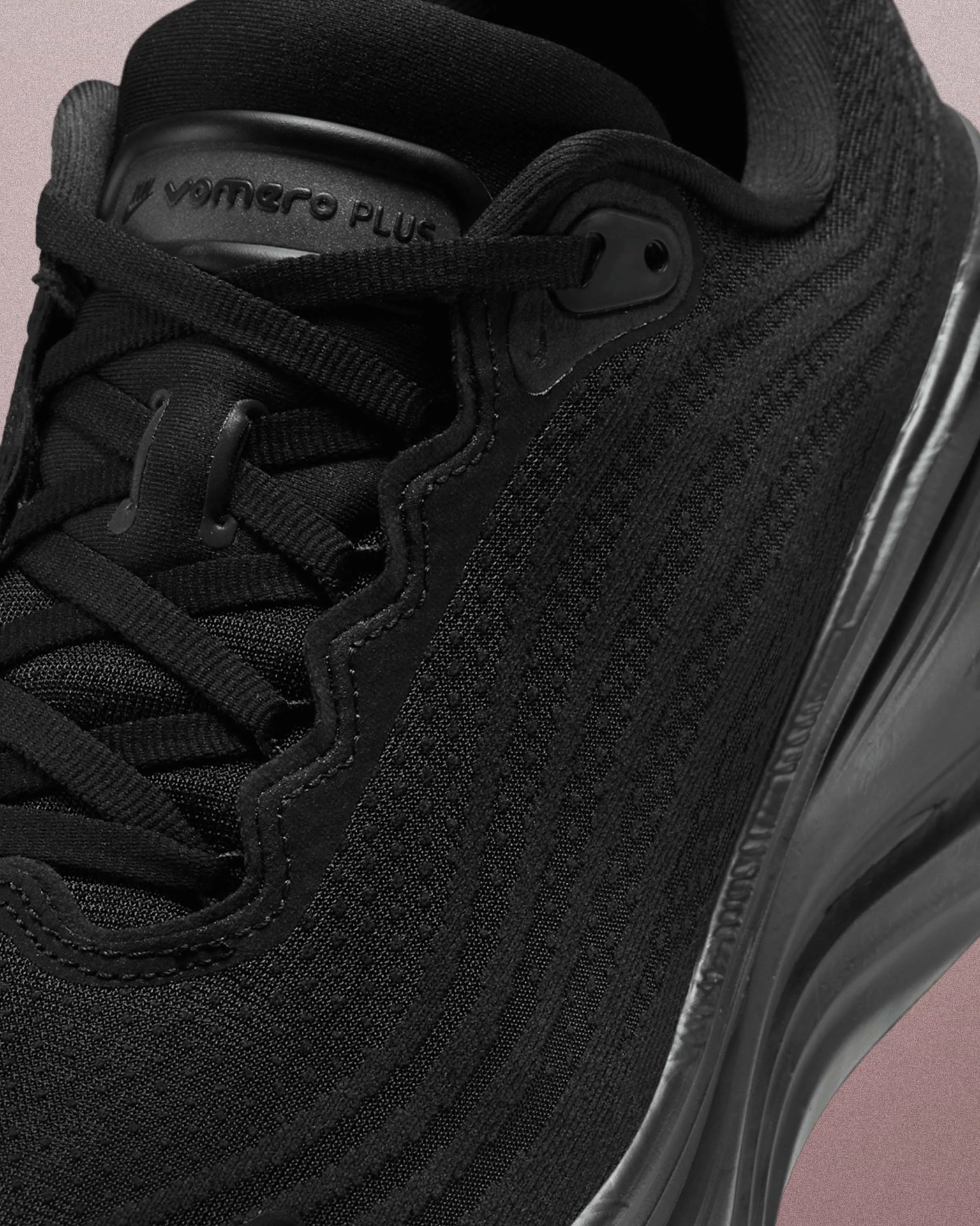 Close-up of a black Vomero Plus sneaker showing textured knit upper, black laces, and cushioned sole.