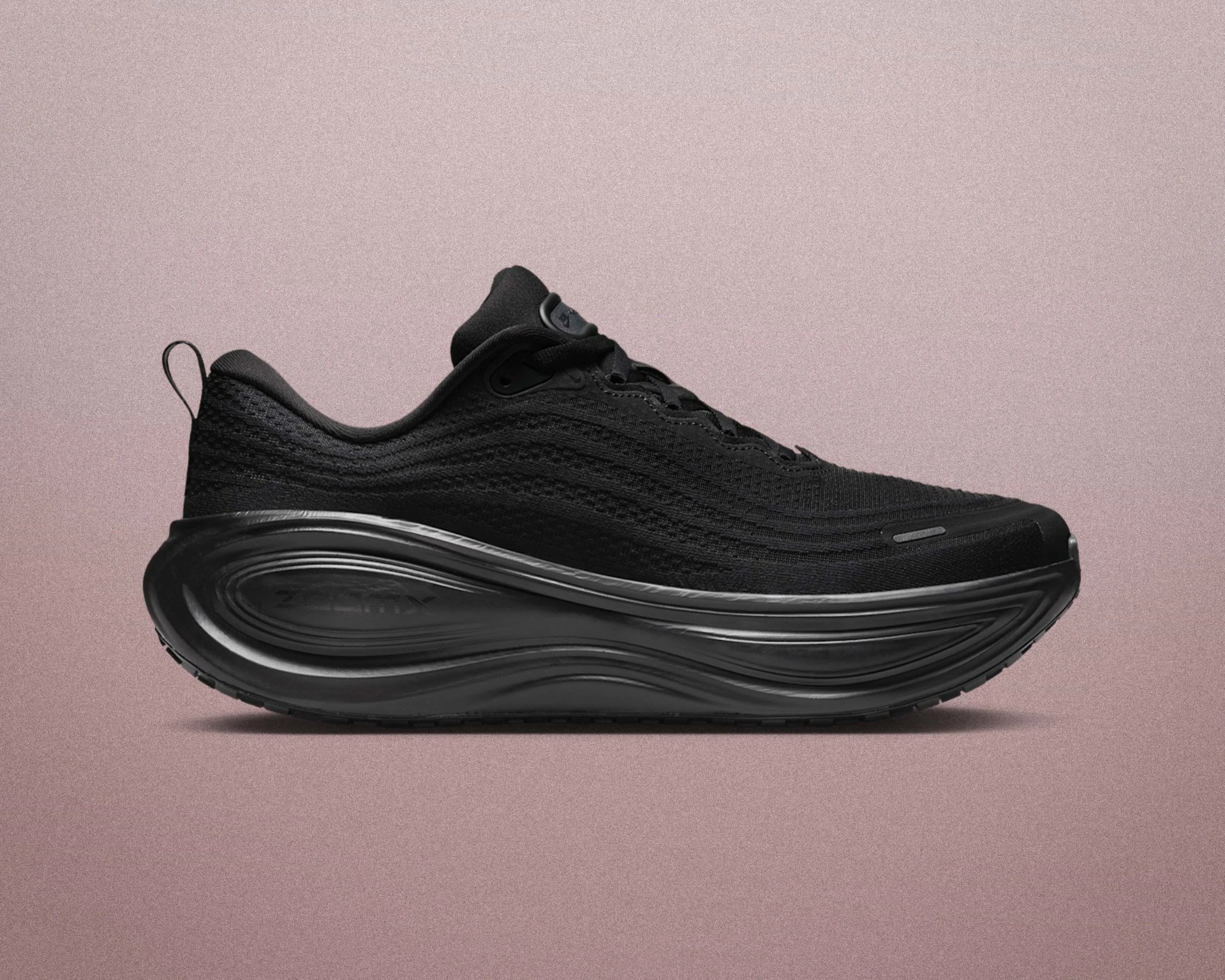 All-black athletic shoe with a thick, sculpted sole and knit upper against a muted pink background.
