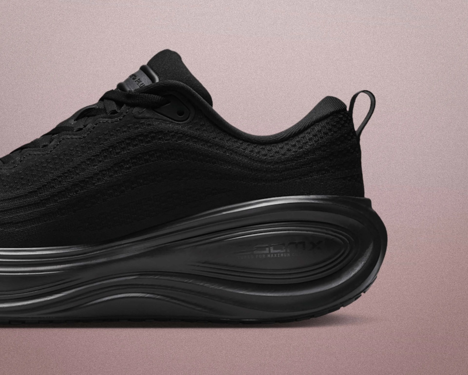 Black athletic sneaker with textured knit upper and thick cushioned sole on a pink background.