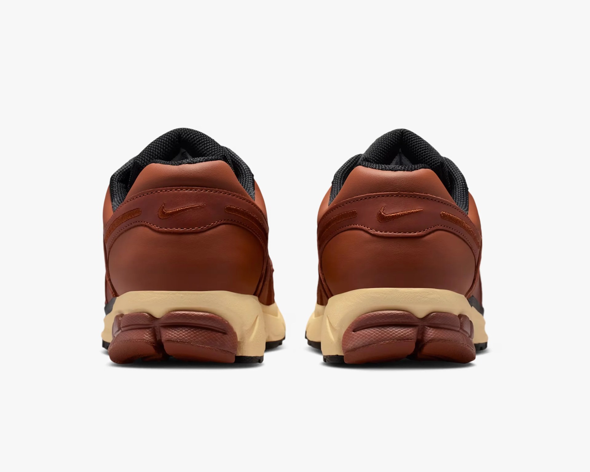 Pair of brown leather Nike sneakers shown from the back with beige midsoles and black inner lining.