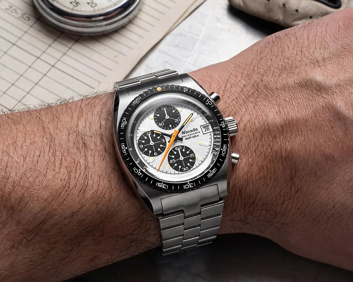 Stainless steel wristwatch with white dial, black subdials, orange second hand, and black bezel on a wrist.