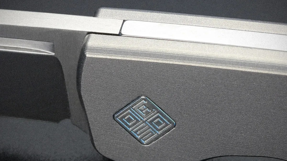 Close-up of a metallic gray folding knife handle with a geometric logo embossed on it.