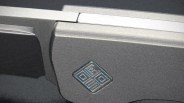 Close-up of a metallic gray folding knife handle with a geometric logo embossed on it.