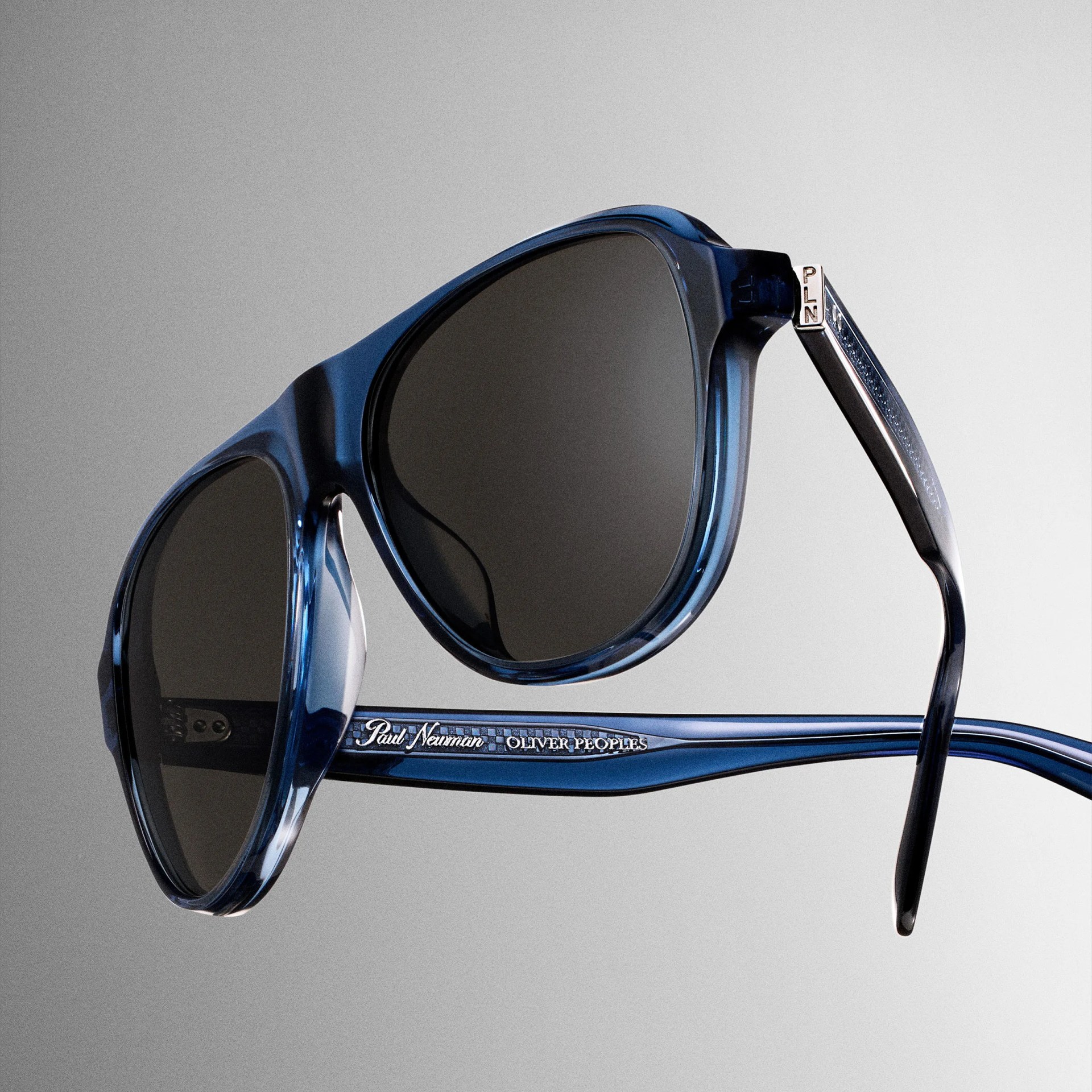 Blue translucent acetate sunglasses with dark lenses and "Paul Newman Oliver Peoples" engraved on the temple.