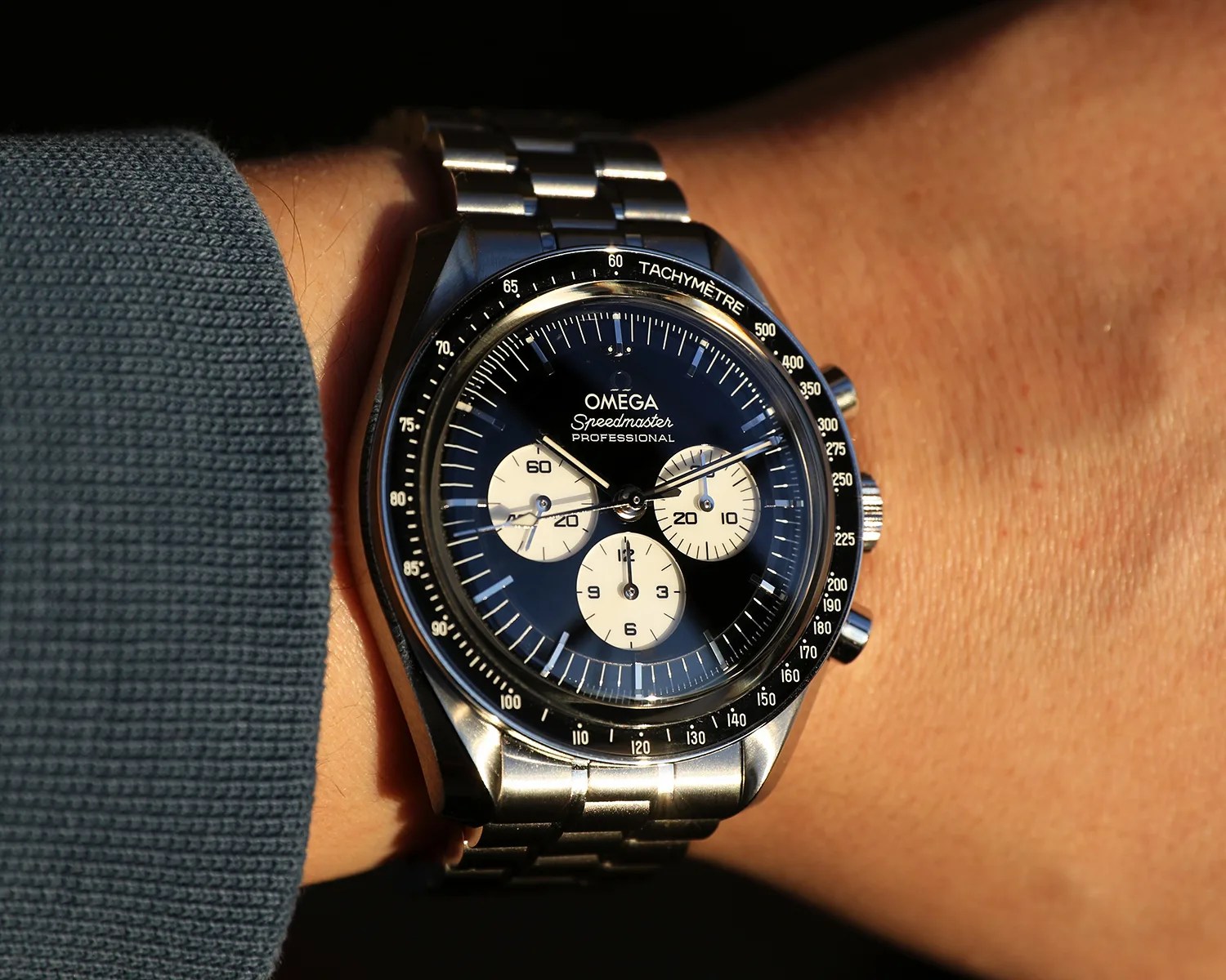 Omega Speedmaster Professional watch with black dial and three white subdials on a metal bracelet worn on a wrist.
