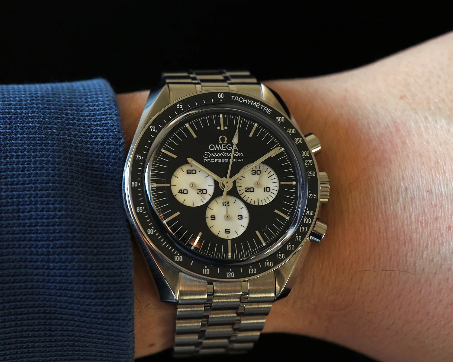 Omega Speedmaster Professional chronograph watch with black dial and stainless steel bracelet on a wrist.