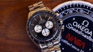 Stainless steel Omega Speedmaster Professional watch with black dial and three white subdials next to a NASA patch.