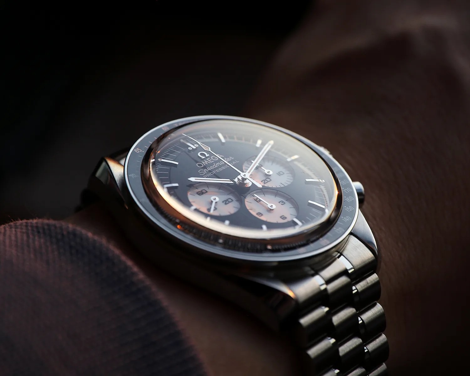 Close-up of a stainless steel Omega Speedmaster Professional watch with black dial and three subdials on a wrist.