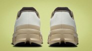 Pair of white and beige athletic shoes with black soles shown from the back on a green background.