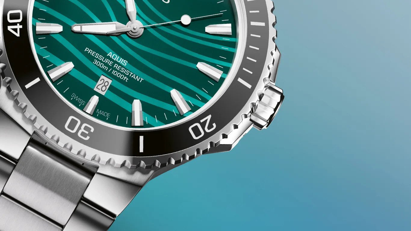 Close-up of a stainless steel wristwatch with a teal patterned dial, black bezel, and date display at 6 o'clock.