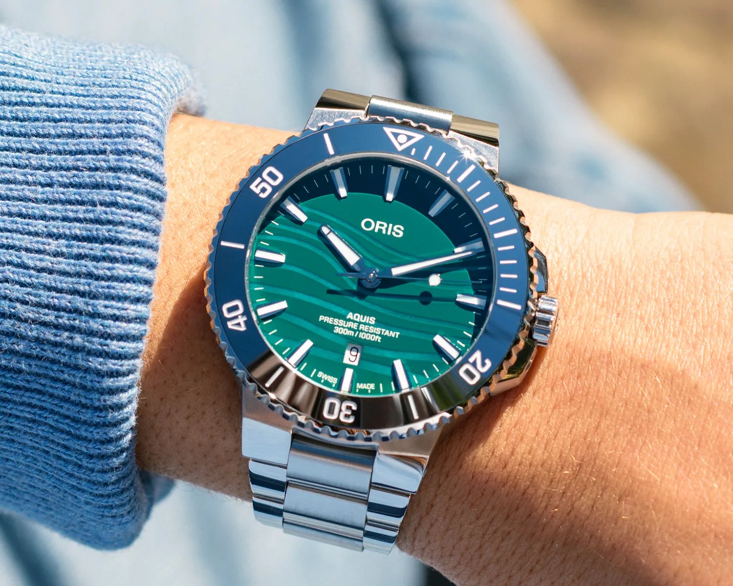 Stainless steel Oris Aquis dive watch with green wave-patterned dial and rotating bezel on a wrist.
