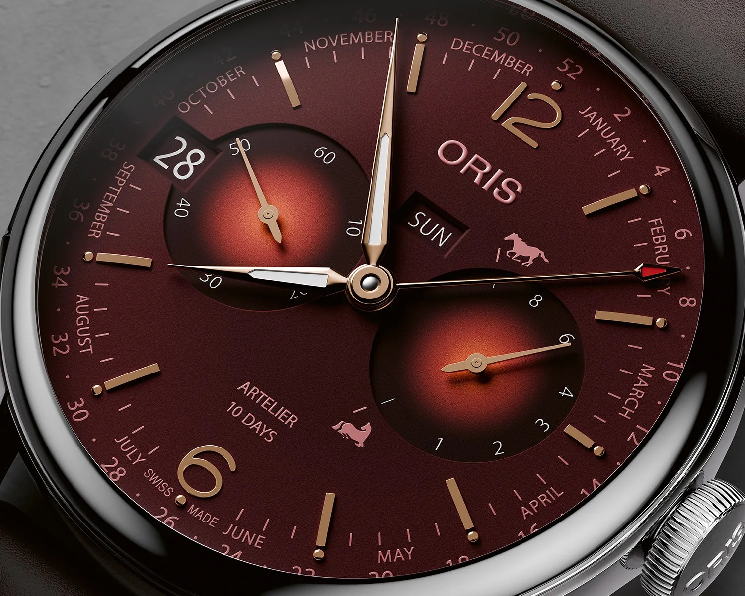Close-up of an Oris Artelier 10 Days watch with a burgundy dial, gold-tone hands and markers, and calendar subdials.