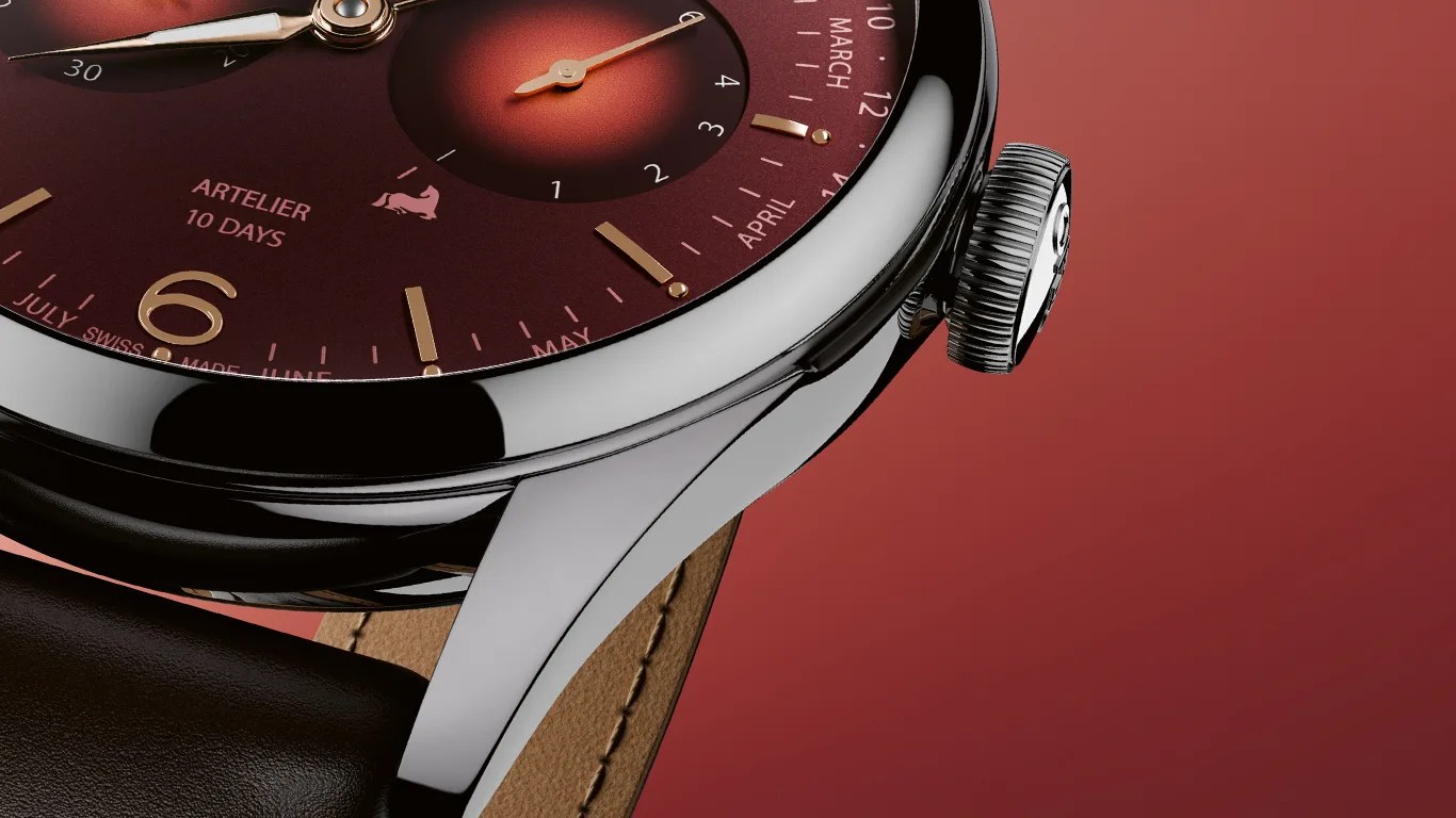 Close-up of a polished silver watch case with a burgundy dial, gold markers, and a brown leather strap.