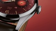 Close-up of a polished silver watch case with a burgundy dial, gold markers, and a brown leather strap.