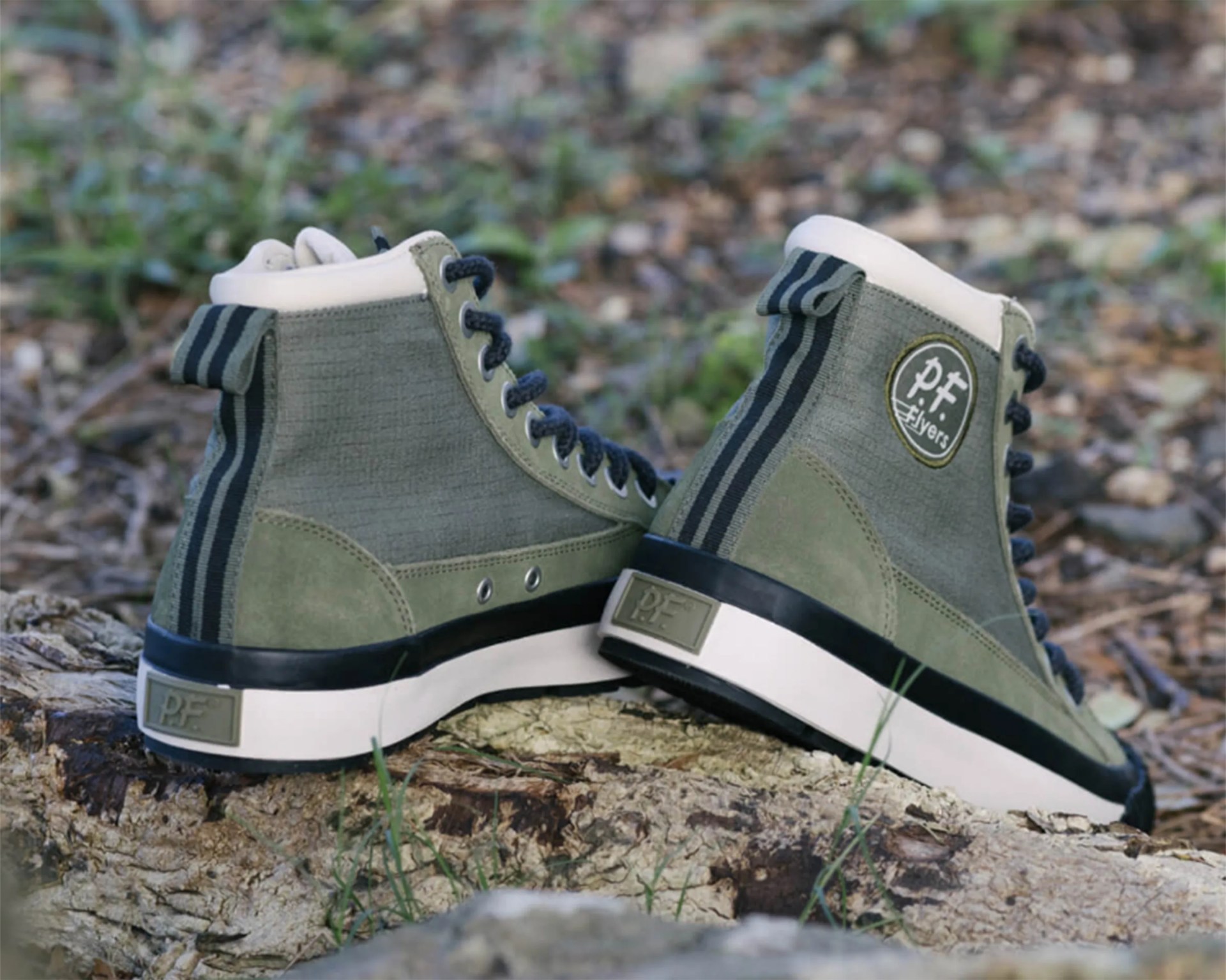 Pair of olive green high-top sneakers with black laces and white soles resting on a log outdoors.