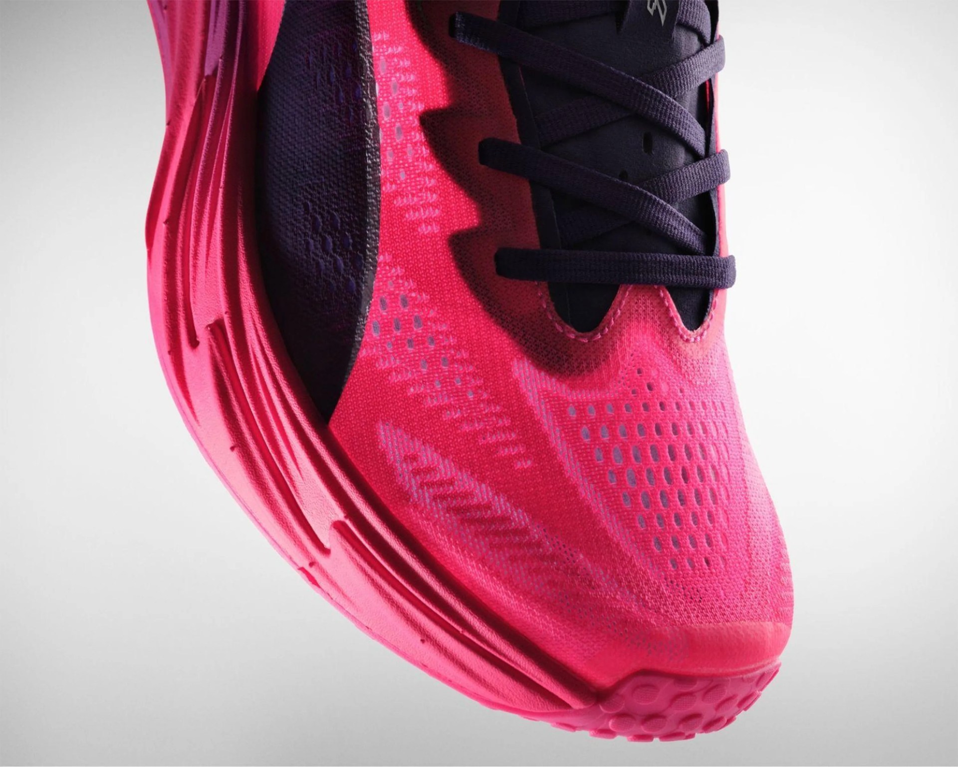 Close-up of a bright pink running shoe with black laces and textured sole.