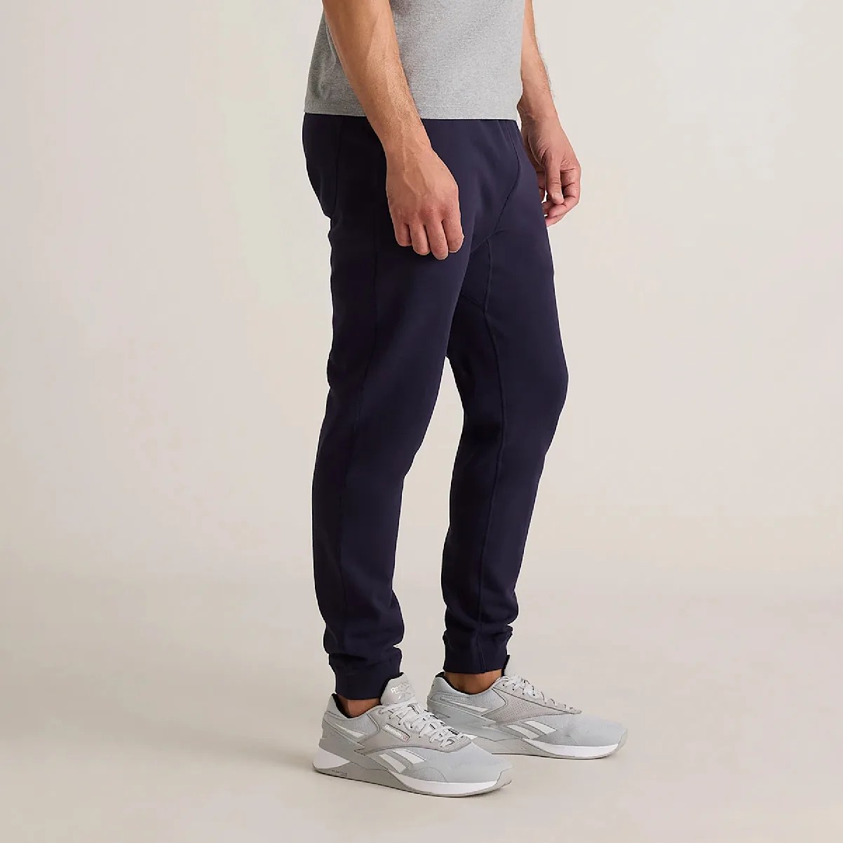 Man wearing navy tapered jogger pants and light gray Reebok sneakers on a neutral background.
