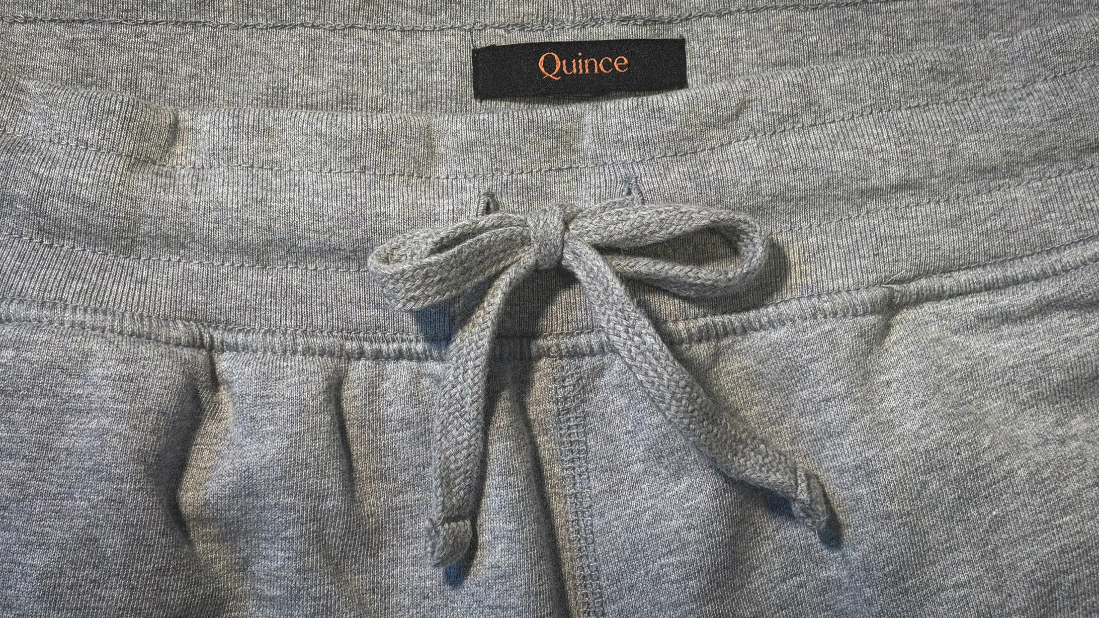 Gray sweatpants waistband with a tied drawstring and a black label reading "Quince.