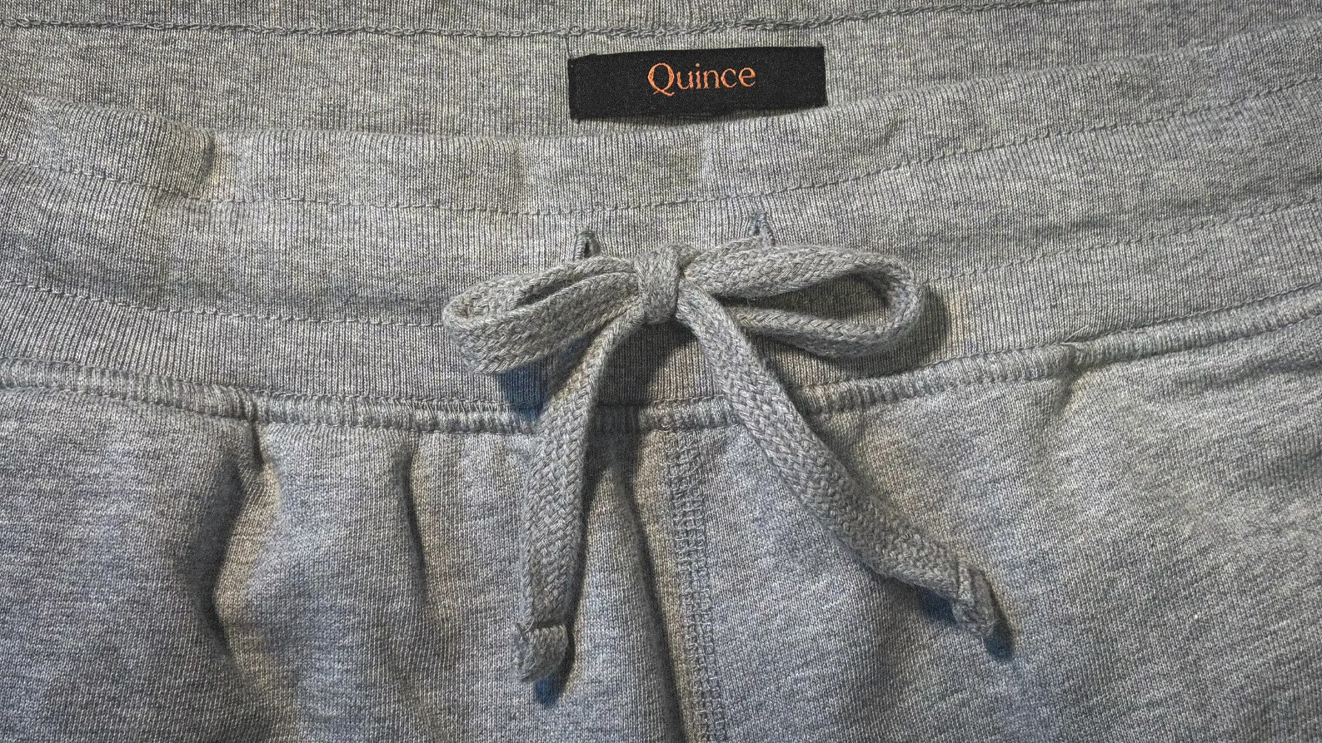 Gray sweatpants waistband with a tied drawstring and a black label reading "Quince.
