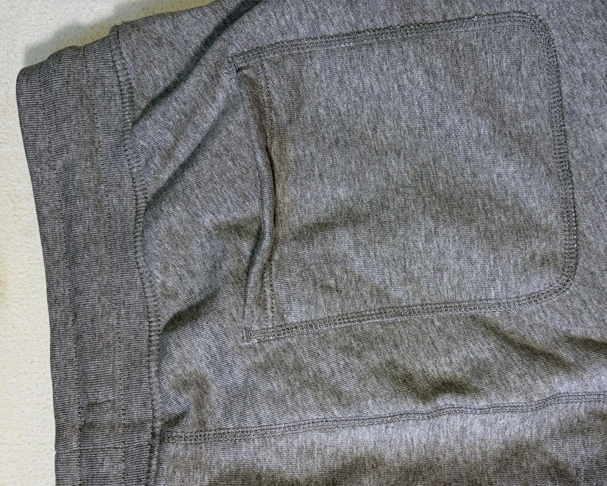 Close-up of a gray fabric pocket with visible stitching on a garment.