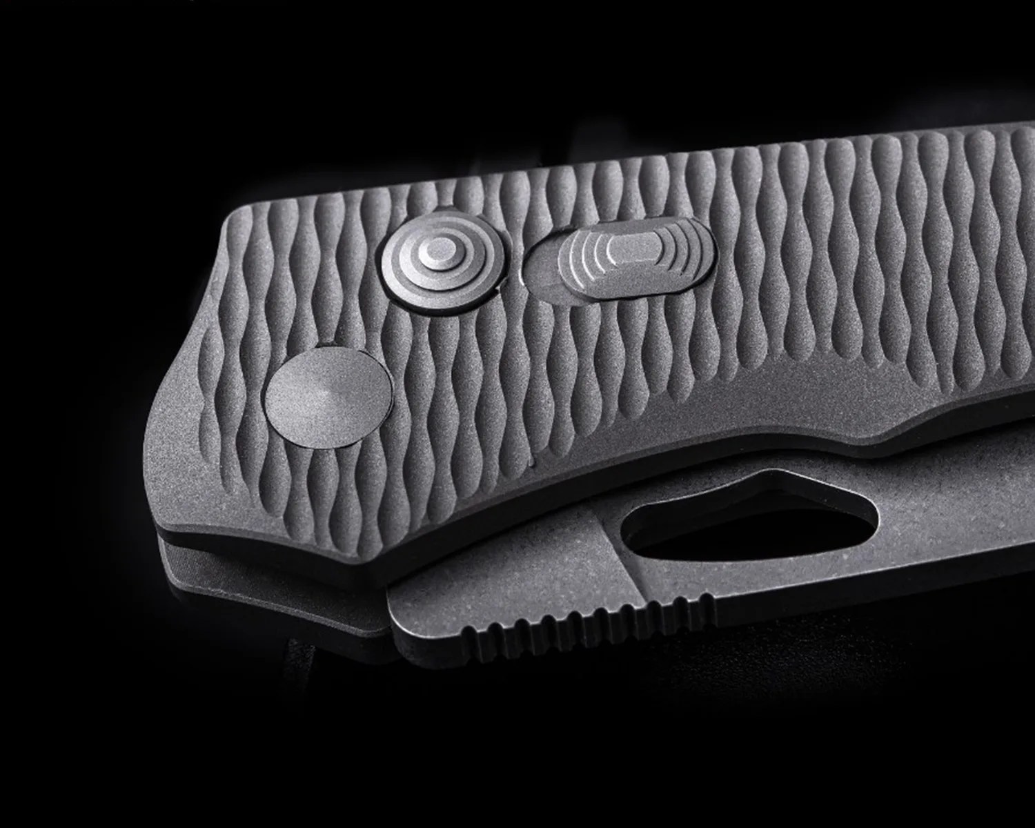 Close-up of a textured gray folding knife handle with circular and oval metal buttons on a black background.