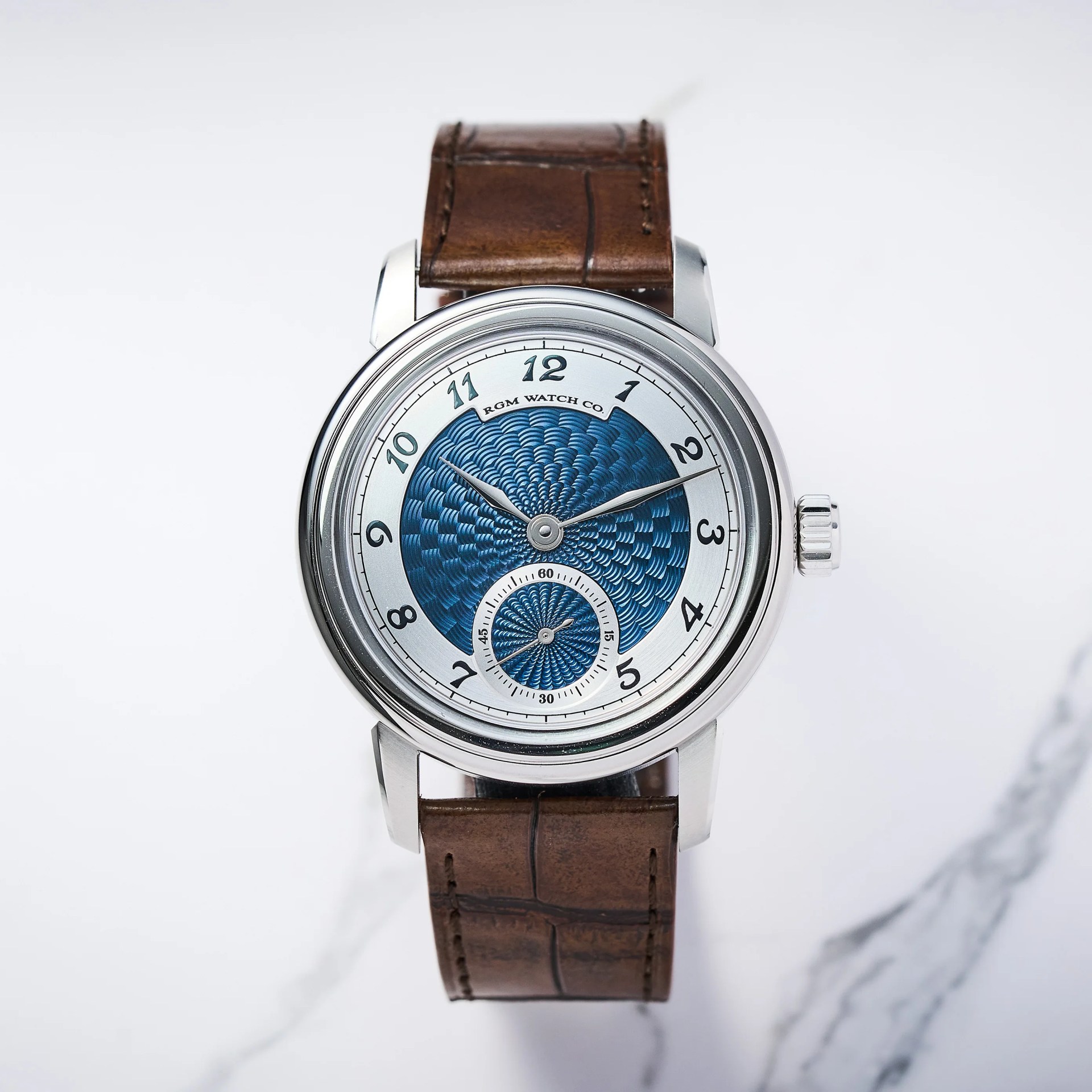 Silver wristwatch with blue guilloch&eacute; dial, black numerals, and brown leather strap on a white marble surface.