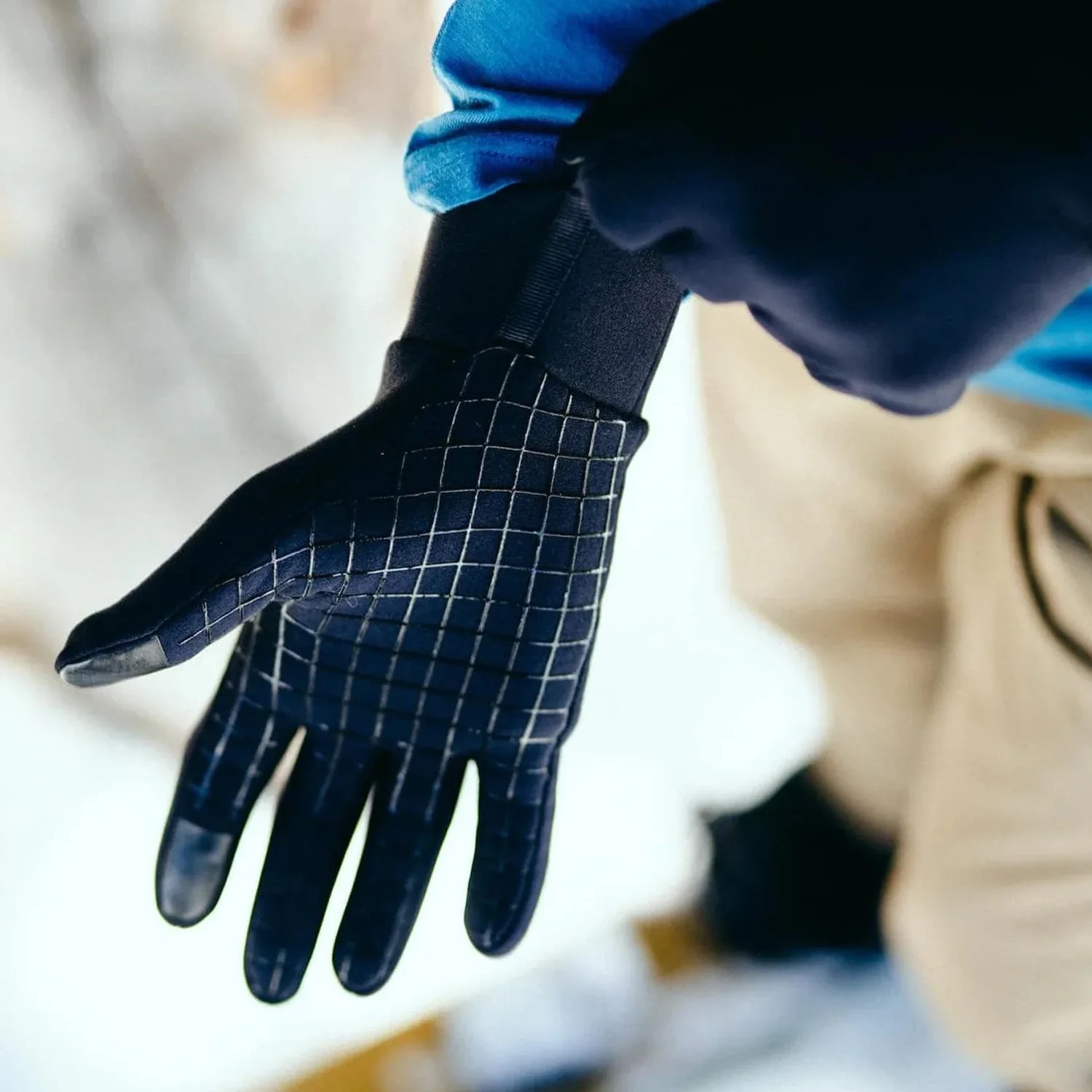 Black glove with a grid pattern and reinforced fingertips worn on a hand.
