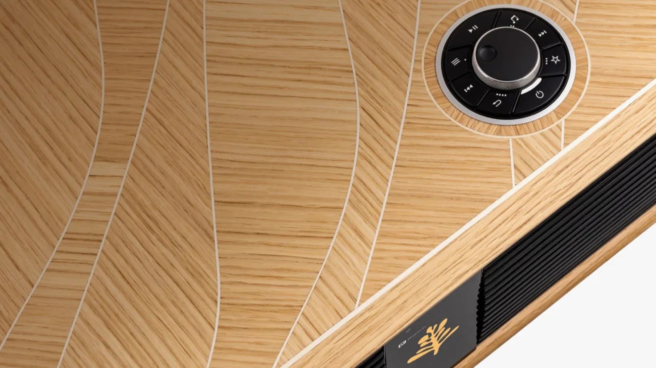 Close-up of a wooden surface with curved inlaid lines, a black circular control knob, and a small display with a yellow logo.