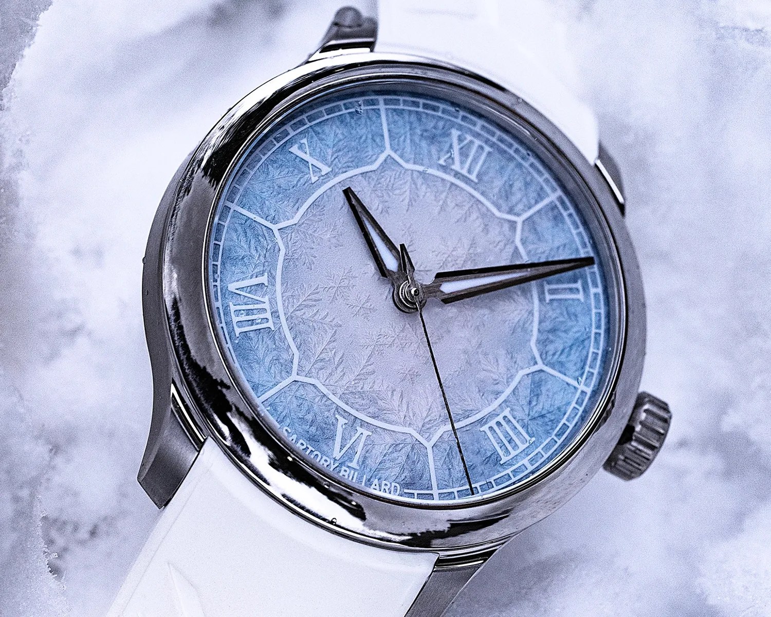 Silver wristwatch with a blue frosted dial, Roman numerals, and a white strap on a snowy surface.