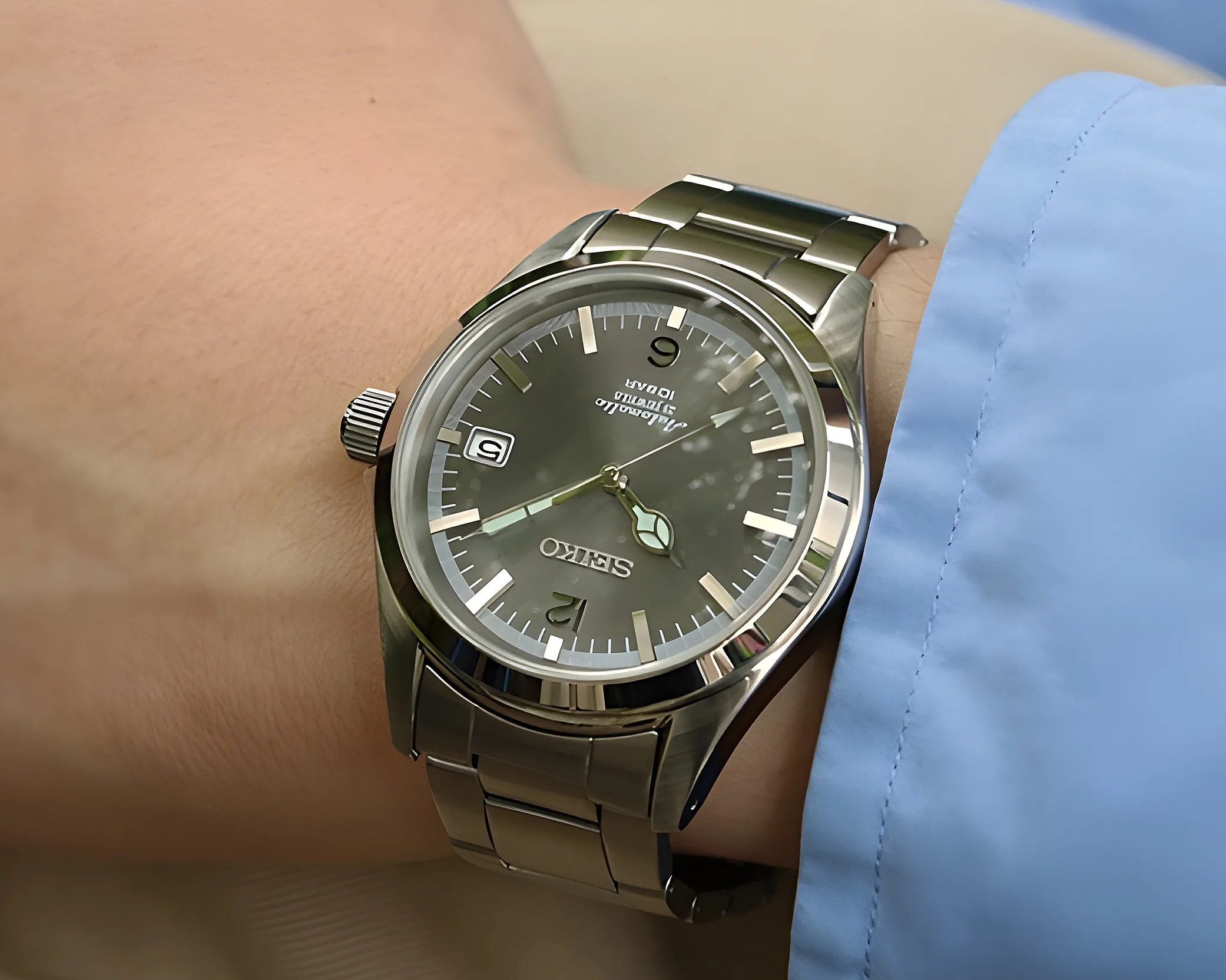 Silver Seiko wristwatch with a dark dial and metal bracelet worn on a wrist with a light blue shirt cuff.