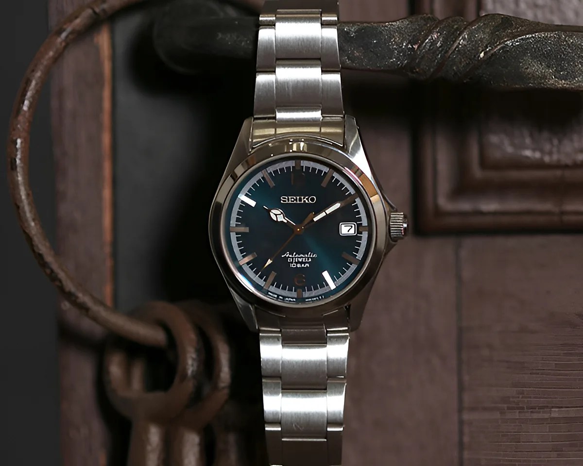 Silver Seiko wristwatch with a blue dial and date display on a metal bracelet hanging on a rustic door handle.