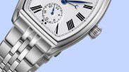 Close-up of a silver metal watch with a white face, black Roman numerals, and blue hands on a light blue background.