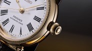 Close-up of a gold-tone Seiko Presage watch with white dial, black Roman numerals, and a ridged crown.