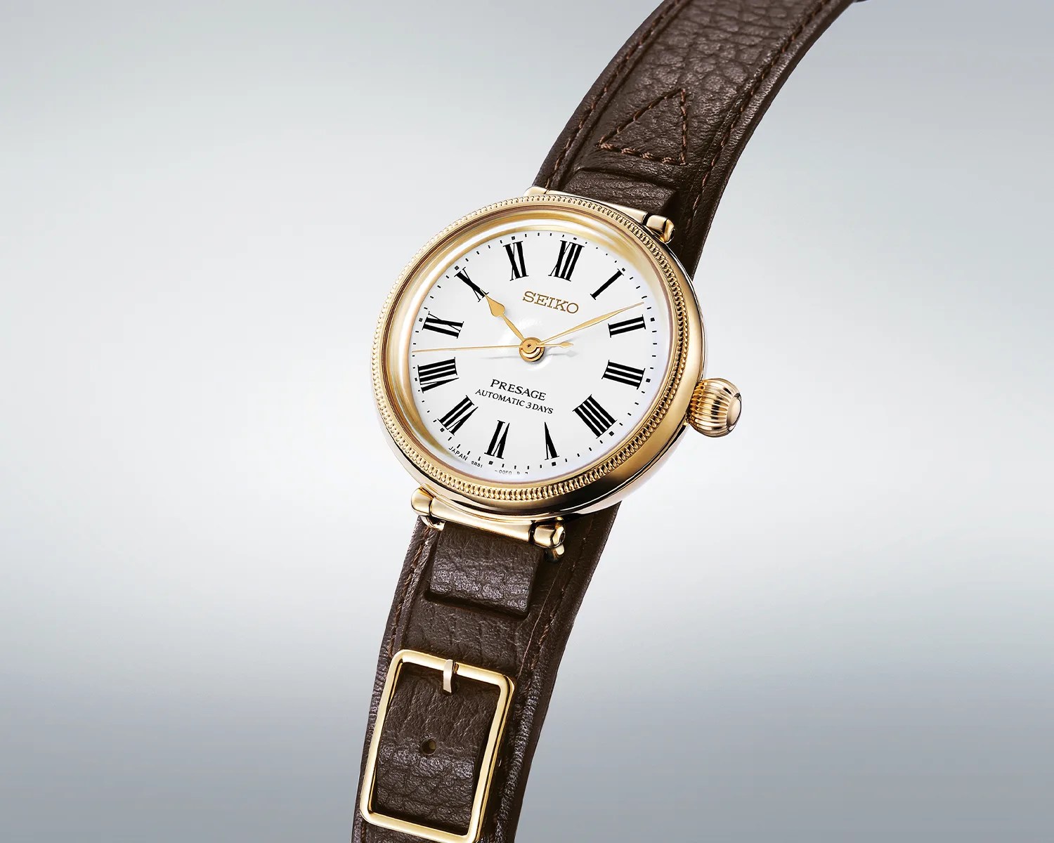 Gold-tone Seiko Presage watch with white dial, black Roman numerals, and brown leather strap.