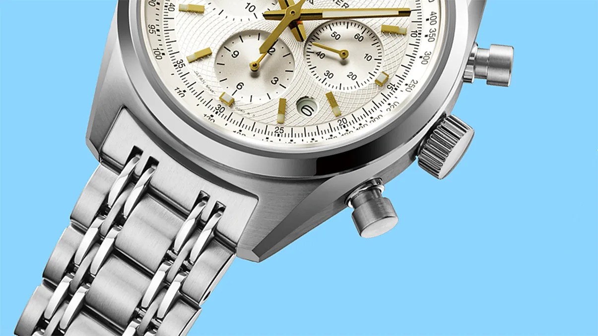 Close-up of a silver stainless steel chronograph watch with a white dial and gold-tone hands and markers on a blue background.