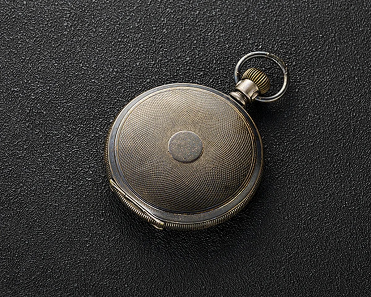 Round vintage silver pocket watch with textured cover on a black textured surface.