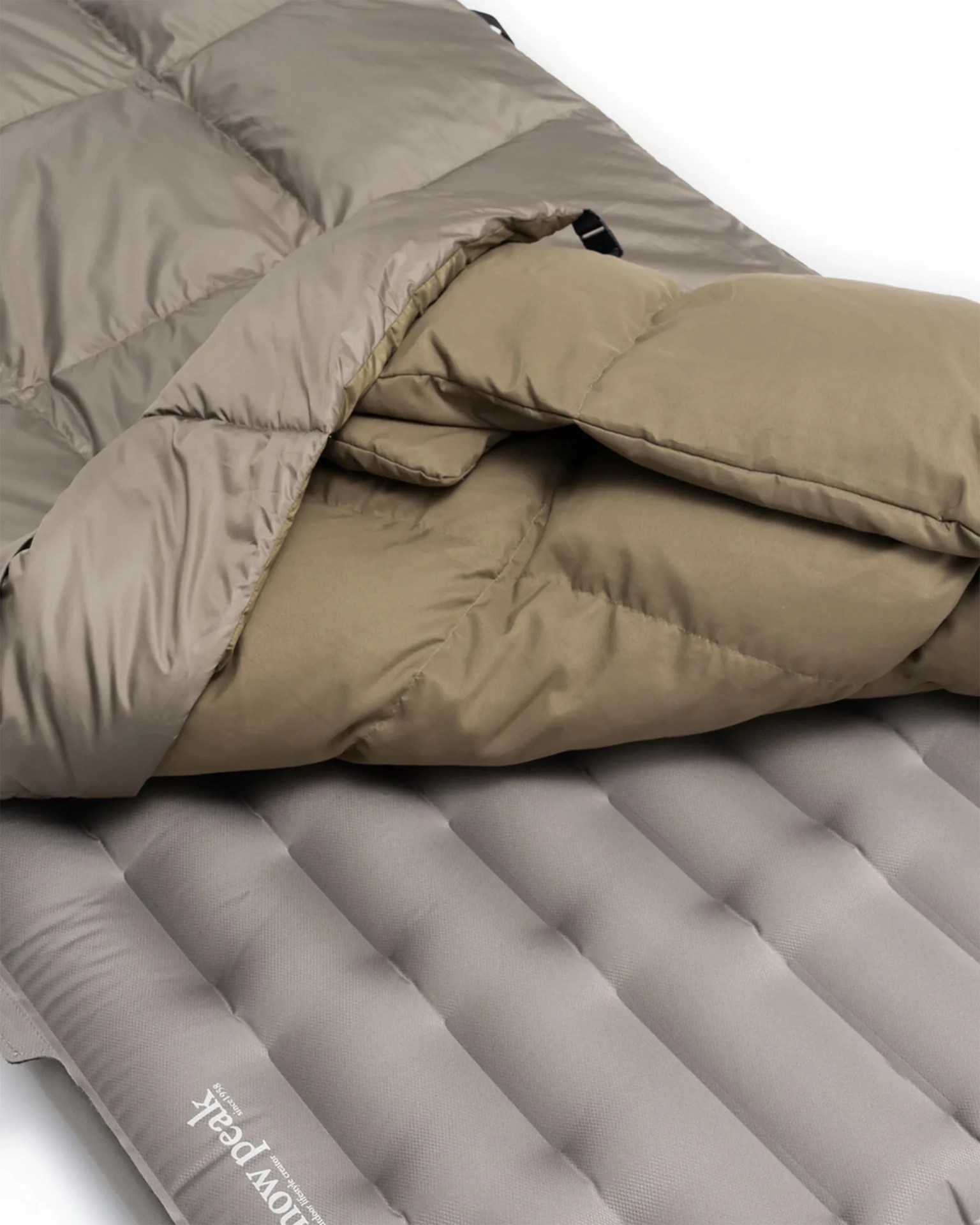 Beige and taupe insulated sleeping bag partially unzipped on a gray inflatable sleeping pad with 