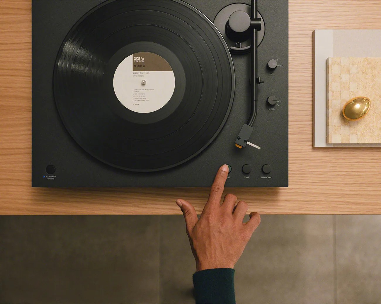 Black turntable with vinyl record on a wooden table, a hand pressing the start button.