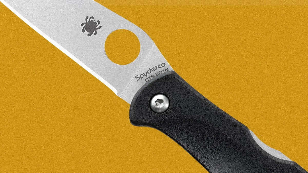 Close-up of a Spyderco folding knife blade with a black handle on a mustard yellow background.