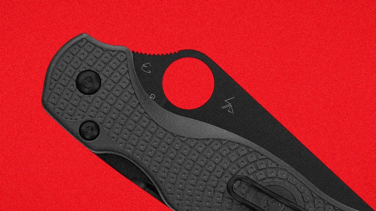 Black folding knife with textured handle and circular thumb hole on a red background.
