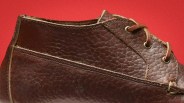 Close-up of a brown textured leather shoe with visible stitching and metal eyelets on a red background.