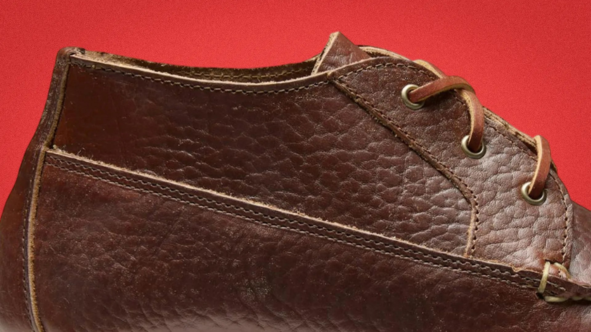 Close-up of a brown textured leather shoe with visible stitching and metal eyelets on a red background.