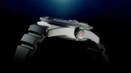 Side view of a silver metal watch case with a black rubber strap and a crown featuring a red circular arrow symbol.