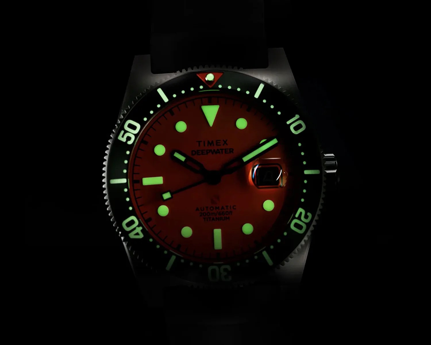 Timex Deepwater watch with glowing green markers and hands on an orange dial and black bezel.